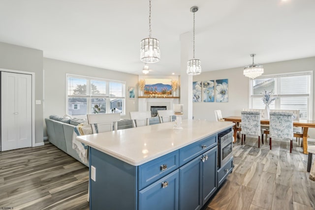 kitchen with stainless steel microwave, blue cabinets, a center island, dark wood-type flooring, and decorative light fixtures