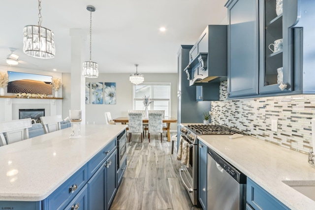 kitchen with light hardwood / wood-style flooring, stainless steel appliances, decorative light fixtures, blue cabinets, and tasteful backsplash