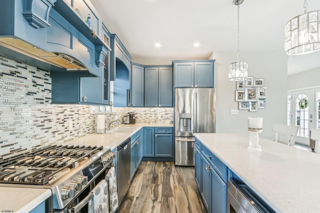 kitchen with decorative backsplash, hanging light fixtures, ventilation hood, blue cabinets, and appliances with stainless steel finishes