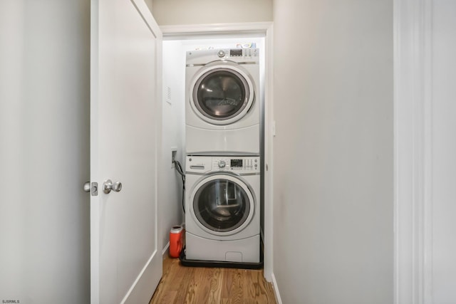 clothes washing area with stacked washer and clothes dryer and light wood-type flooring