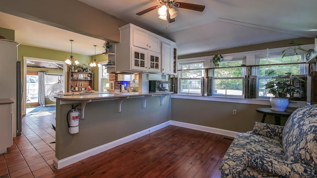 kitchen with kitchen peninsula, a kitchen breakfast bar, decorative light fixtures, white cabinets, and dark wood-type flooring