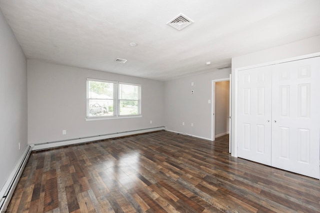 unfurnished bedroom with dark wood-type flooring, a closet, and a baseboard heating unit