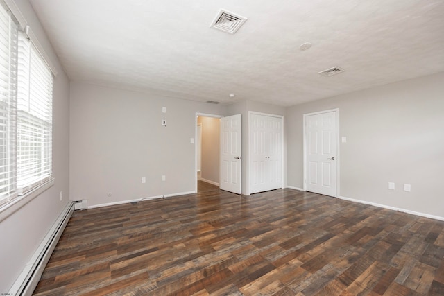 empty room with dark wood-type flooring, a textured ceiling, and a baseboard heating unit