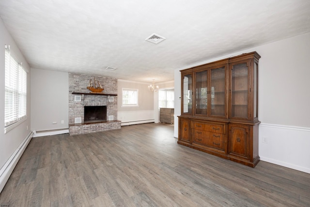 unfurnished living room featuring a large fireplace, a notable chandelier, a baseboard heating unit, and dark hardwood / wood-style flooring