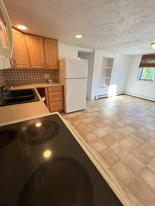 kitchen with a textured ceiling, white refrigerator, backsplash, and sink