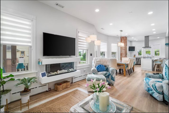 living room featuring baseboard heating, sink, and light wood-type flooring