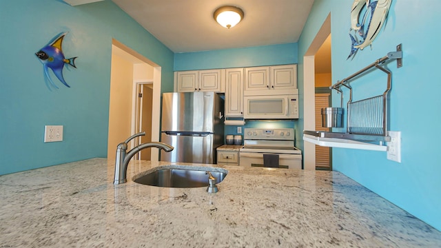 kitchen with sink, light stone countertops, stainless steel appliances, and cream cabinets