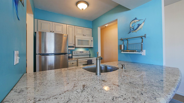 kitchen with stainless steel appliances, light stone countertops, sink, and kitchen peninsula