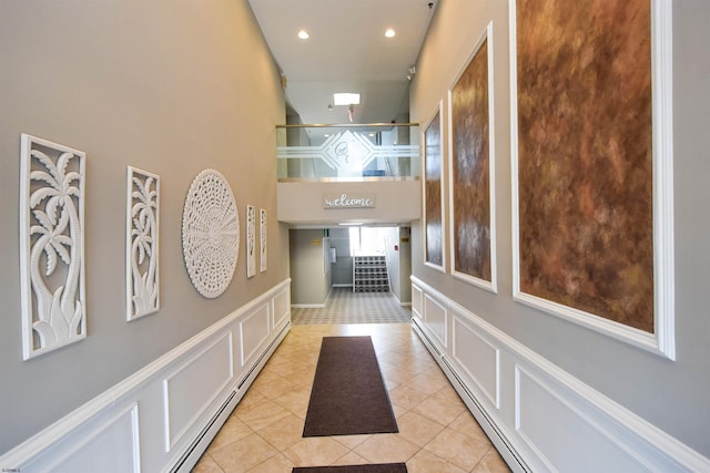 hall with light tile patterned flooring, a high ceiling, and a baseboard heating unit