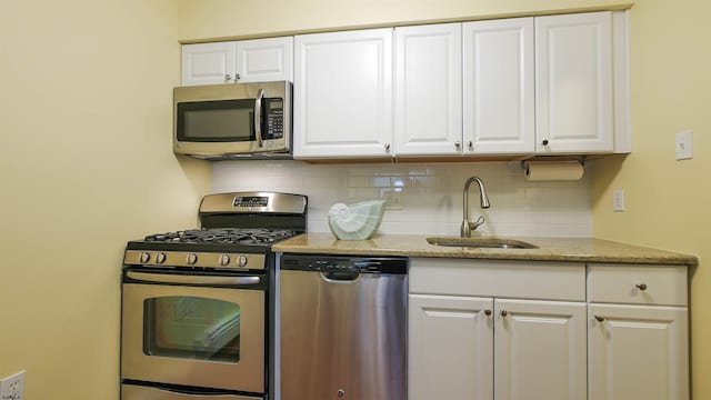 kitchen with appliances with stainless steel finishes, white cabinetry, sink, and backsplash