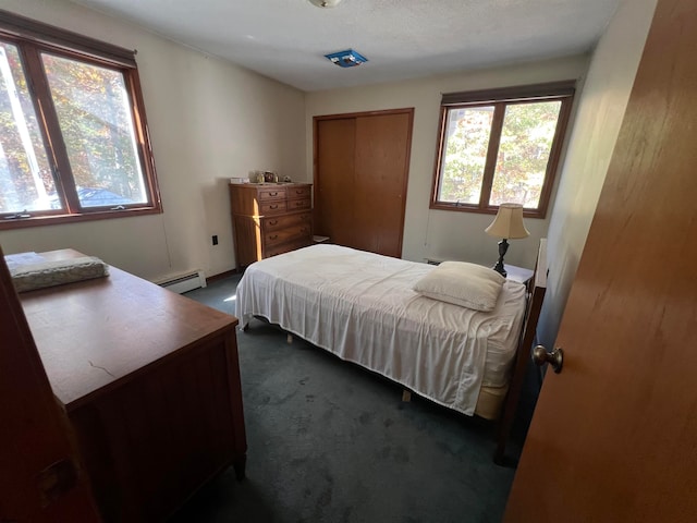 bedroom with a baseboard heating unit, a closet, a textured ceiling, and dark carpet