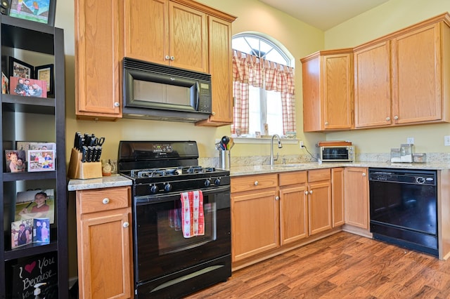 kitchen with sink, black appliances, light hardwood / wood-style flooring, and light stone counters