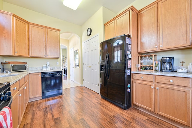 kitchen with ornamental molding, black appliances, dark wood-type flooring, and light stone counters