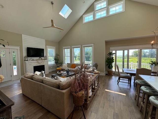 living room featuring hardwood / wood-style floors, high vaulted ceiling, a skylight, ceiling fan, and a large fireplace