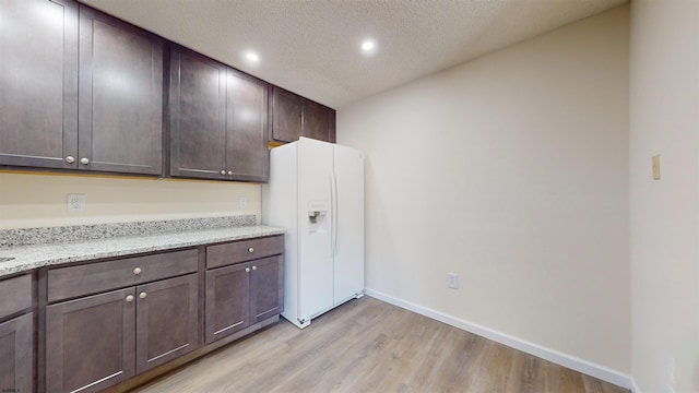 kitchen with white fridge with ice dispenser, a textured ceiling, light hardwood / wood-style floors, dark brown cabinetry, and light stone counters