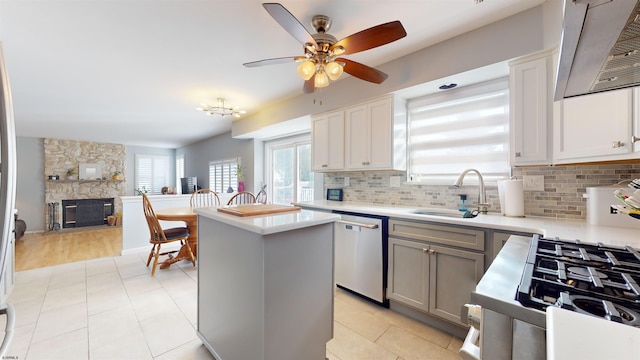 kitchen featuring decorative backsplash, stainless steel dishwasher, sink, a stone fireplace, and a center island