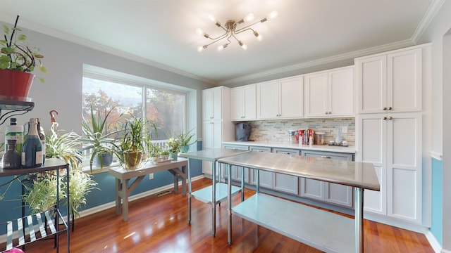 kitchen with wood-type flooring, backsplash, ornamental molding, a chandelier, and white cabinetry