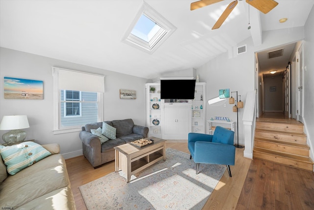 living room featuring lofted ceiling with skylight, light hardwood / wood-style floors, and ceiling fan