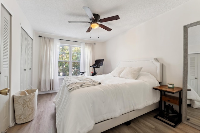 bedroom with multiple closets, a textured ceiling, wood-type flooring, and ceiling fan