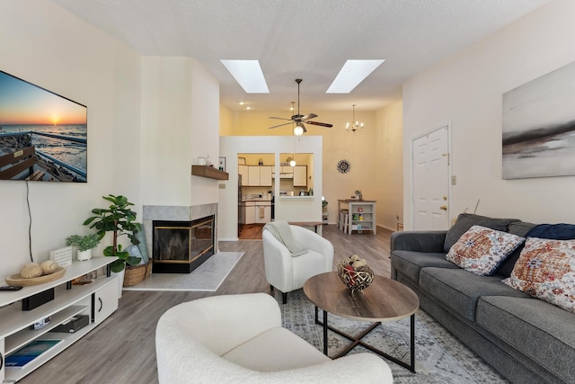 living room with dark wood-type flooring, a textured ceiling, a multi sided fireplace, and ceiling fan with notable chandelier