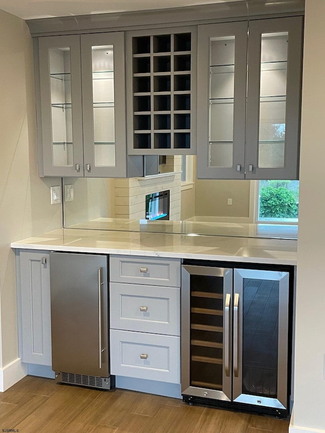 bar featuring gray cabinetry, backsplash, stainless steel fridge, light hardwood / wood-style floors, and wine cooler