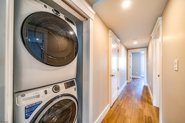 clothes washing area with light hardwood / wood-style flooring and stacked washer and dryer