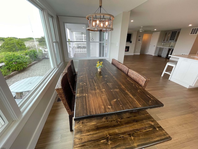 dining room featuring hardwood / wood-style floors, ceiling fan with notable chandelier, and a fireplace