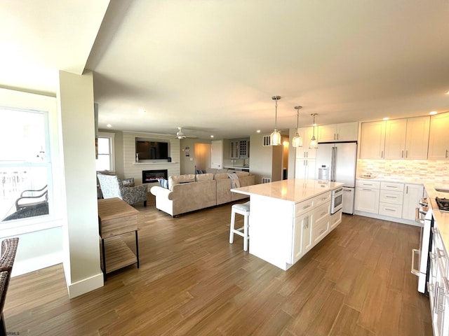 kitchen featuring white cabinets, a large fireplace, appliances with stainless steel finishes, a kitchen bar, and a center island