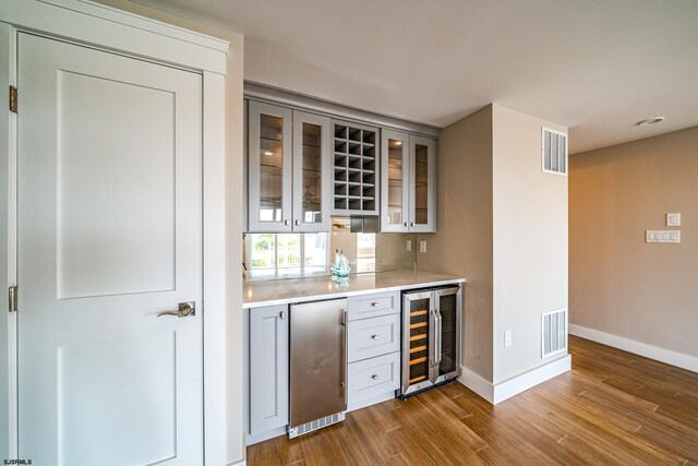 bar with stainless steel refrigerator, dark hardwood / wood-style floors, and beverage cooler