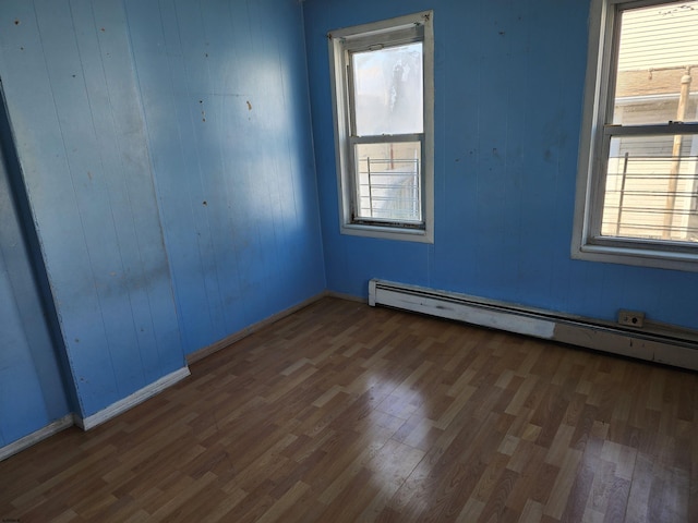 spare room featuring a baseboard radiator, wood walls, and dark hardwood / wood-style flooring