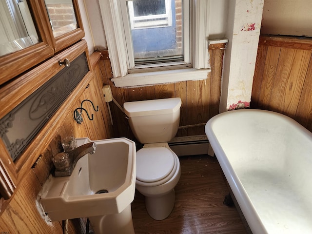 bathroom with a baseboard radiator, wood-type flooring, toilet, wooden walls, and sink