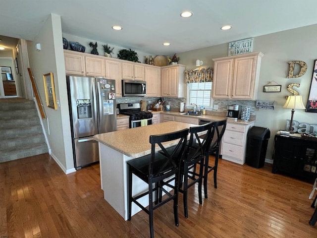 kitchen with appliances with stainless steel finishes, sink, a center island, hardwood / wood-style floors, and a kitchen breakfast bar