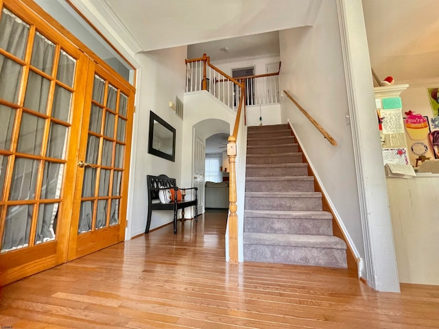 stairway with ornamental molding, french doors, and wood-type flooring