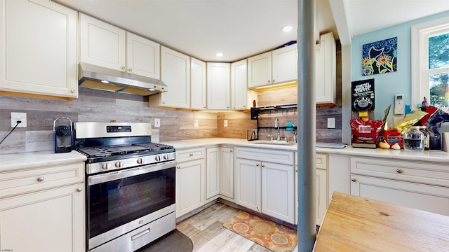 kitchen with sink, stainless steel gas range oven, white cabinets, and light wood-type flooring