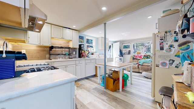 kitchen with tasteful backsplash, sink, light wood-type flooring, white cabinets, and white fridge