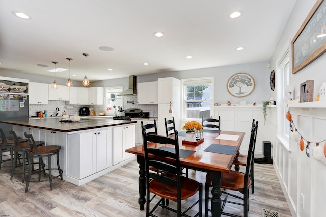 kitchen with wall chimney exhaust hood, light hardwood / wood-style flooring, sink, pendant lighting, and white cabinets