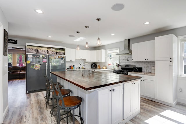 kitchen featuring wall chimney range hood, gas stove, a healthy amount of sunlight, and butcher block counters