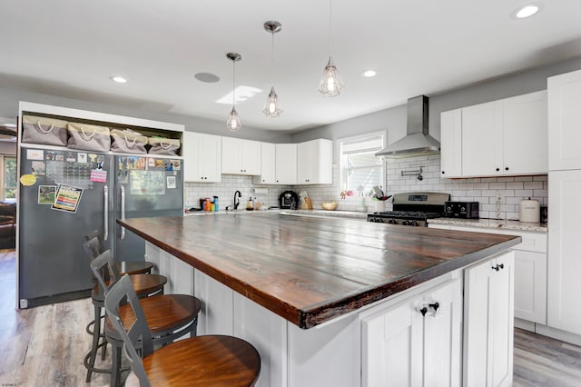 kitchen with wood counters, wall chimney range hood, stainless steel gas range, and white cabinets