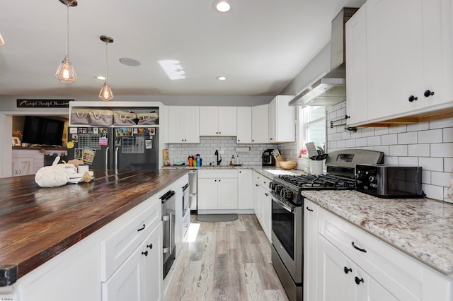 kitchen with butcher block counters, black fridge, light hardwood / wood-style flooring, stainless steel gas range, and white cabinets