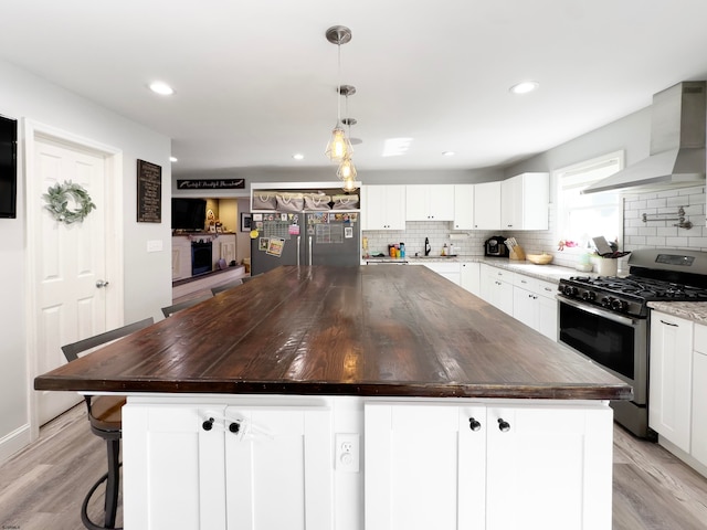 kitchen with appliances with stainless steel finishes, wall chimney exhaust hood, white cabinetry, and a kitchen island