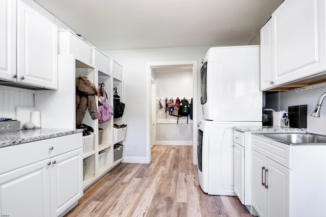 kitchen featuring white cabinets, light stone counters, stacked washer and dryer, light hardwood / wood-style floors, and sink