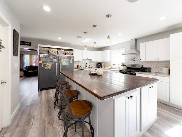 kitchen featuring wall chimney range hood, a kitchen island, plenty of natural light, and stainless steel range with gas stovetop