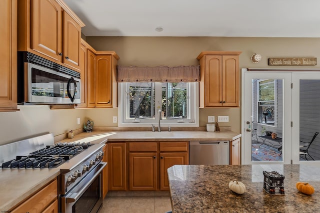 kitchen with dark stone countertops, stainless steel appliances, sink, and light tile patterned floors