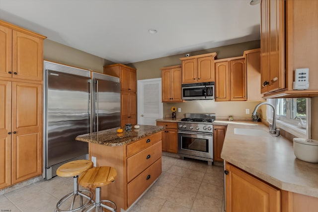 kitchen with sink, a kitchen island, high quality appliances, a breakfast bar area, and light tile patterned floors