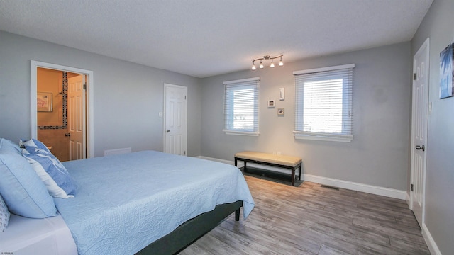 bedroom featuring connected bathroom, hardwood / wood-style floors, and a textured ceiling