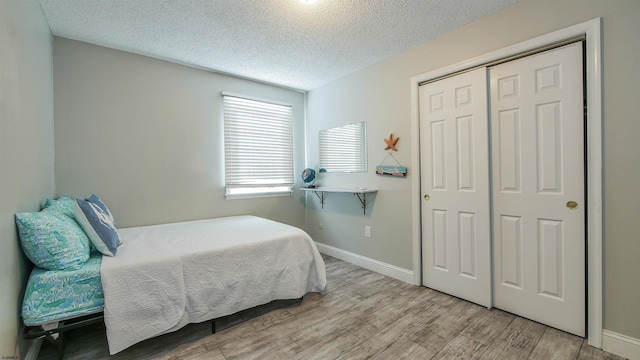 bedroom with light hardwood / wood-style flooring, a textured ceiling, and a closet