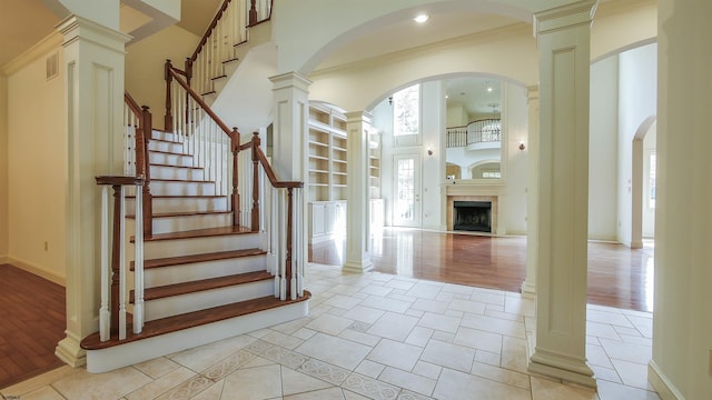 foyer entrance featuring ornate columns, a towering ceiling, and light wood-type flooring