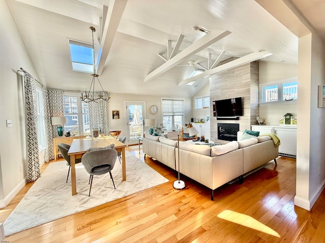 living room featuring vaulted ceiling with skylight, hardwood / wood-style floors, a tiled fireplace, and a chandelier