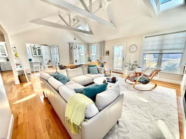 living room featuring a skylight, light wood-type flooring, beam ceiling, high vaulted ceiling, and an inviting chandelier