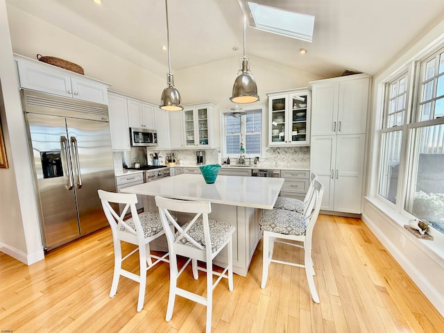 kitchen featuring hanging light fixtures, backsplash, vaulted ceiling with skylight, a center island, and premium appliances